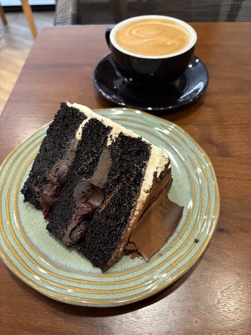 A slice of rich chocolate cake with cream frosting and a cup of latte art coffee.