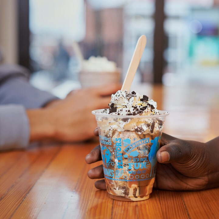 A hand holds a Ben & Jerry's ice cream sundae topped with whipped cream and cookie crumbles.