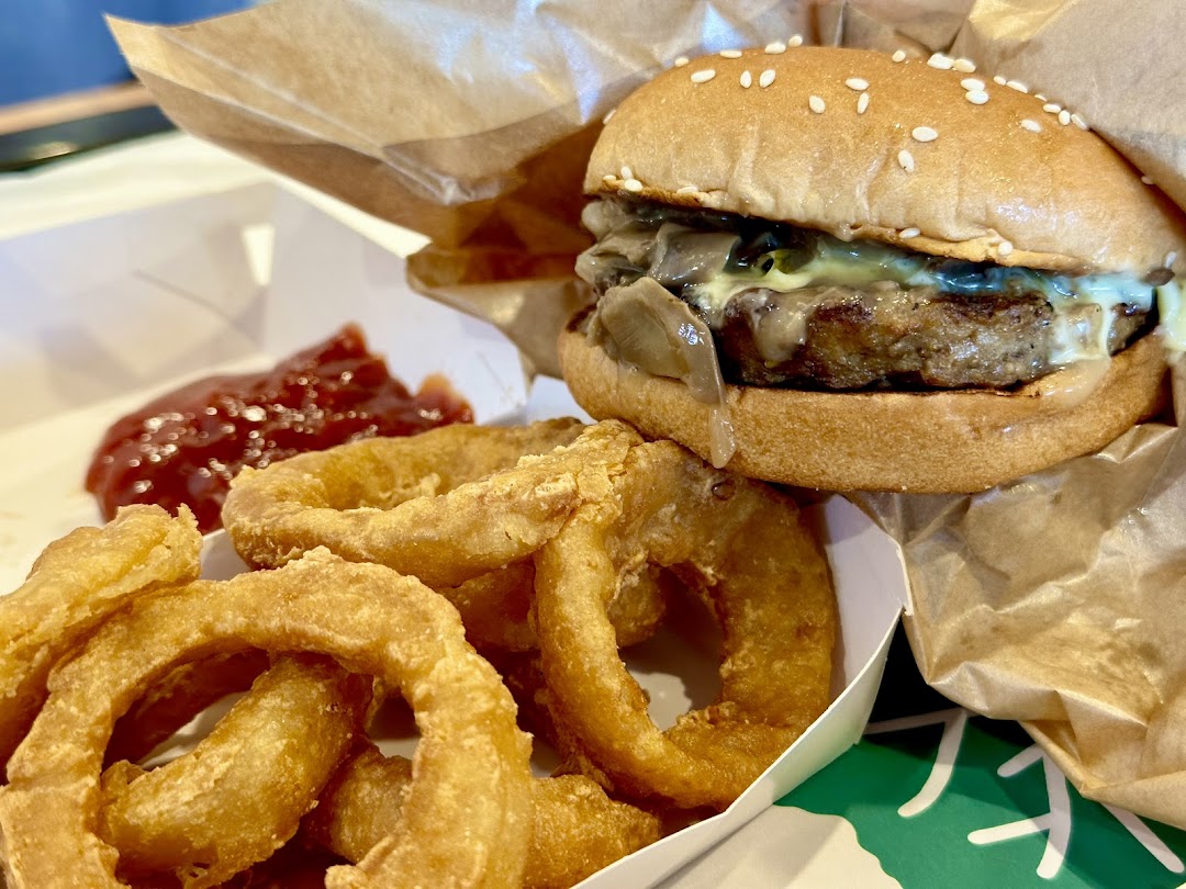 A close-up shot of a juicy mushroom and swiss burger with onion rings and ketchup.