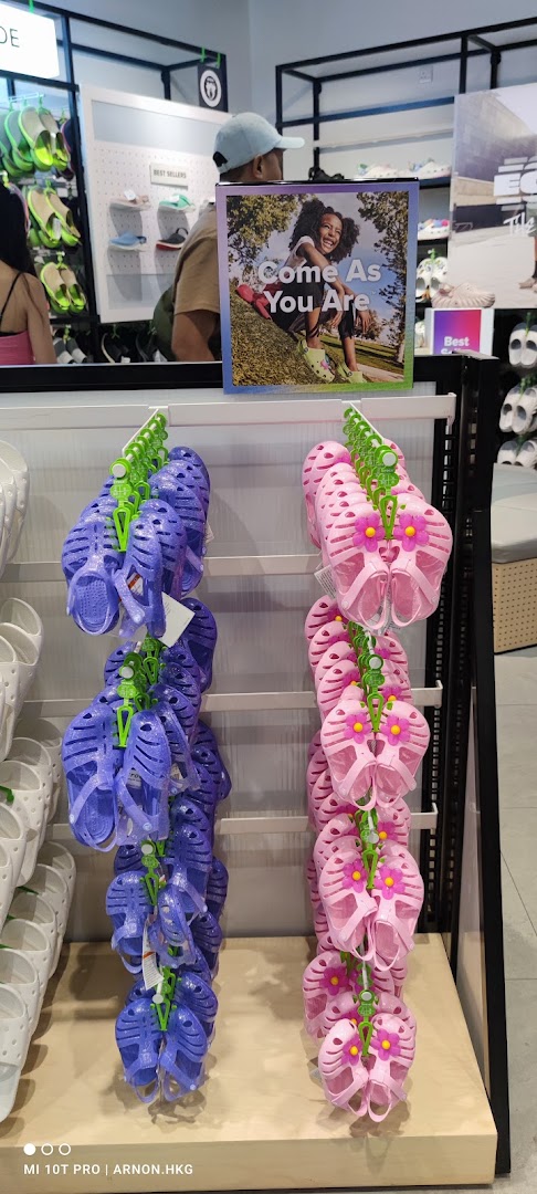 A display of colorful Crocs sandals, featuring purple and pink styles, with a motivational poster.