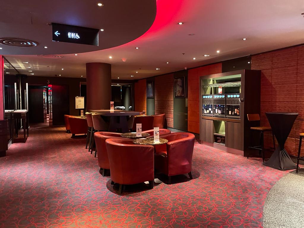 Interior of a lounge area with red seating, tables, and a display of beverages.