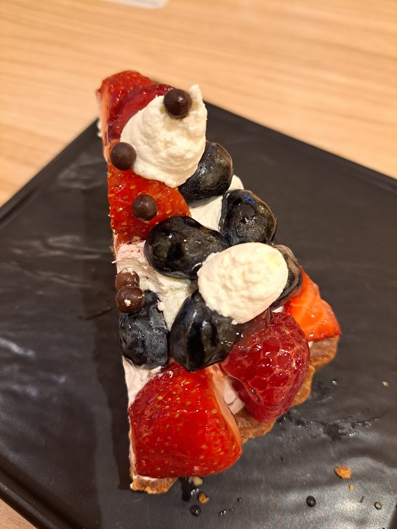A slice of fruit tart topped with strawberries, blueberries, whipped cream, and chocolate balls.