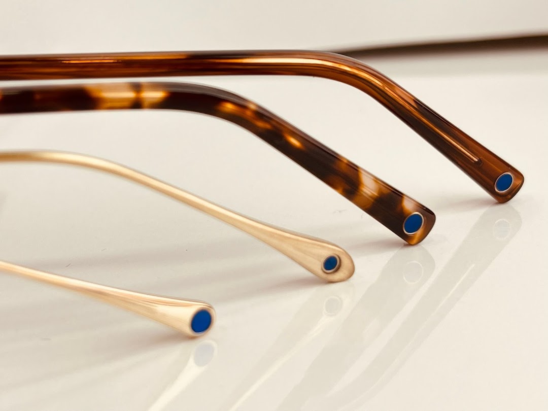 Close-up of the temple tips of three pairs of eyeglasses, showcasing different materials and designs.