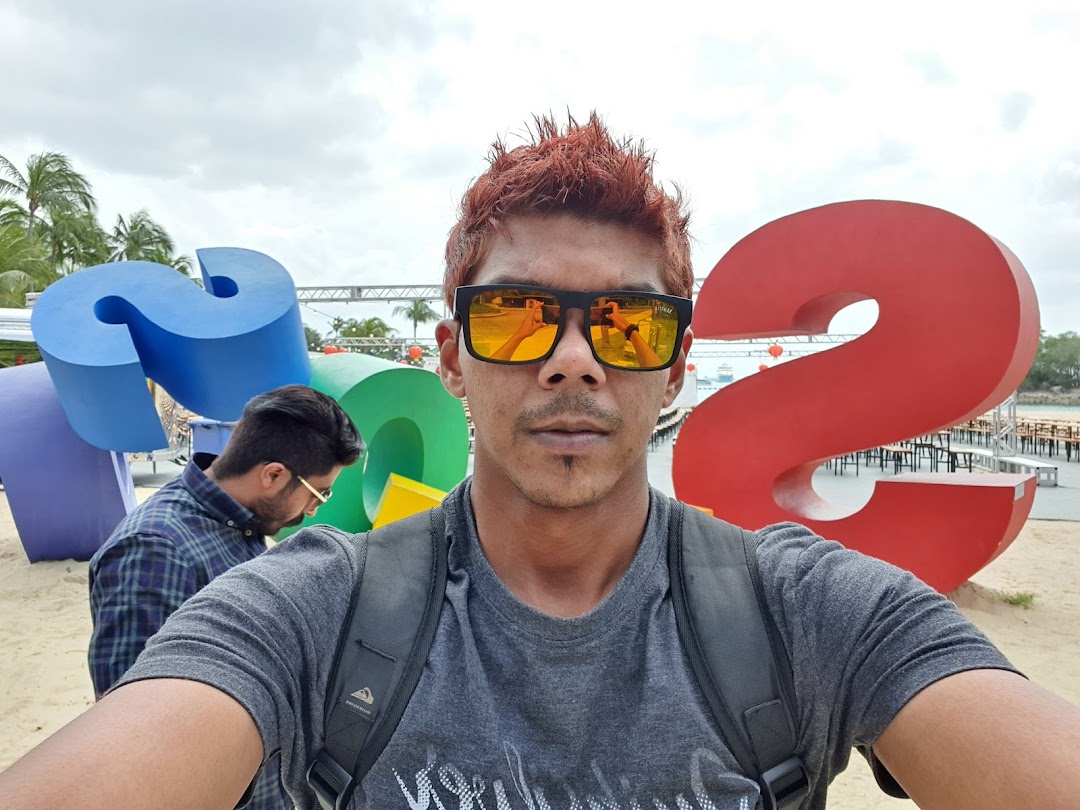 A man takes a selfie in front of large colorful numbers on a beach.