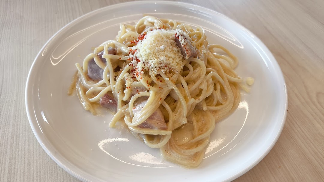 A plate of spaghetti carbonara topped with grated cheese and red pepper flakes.