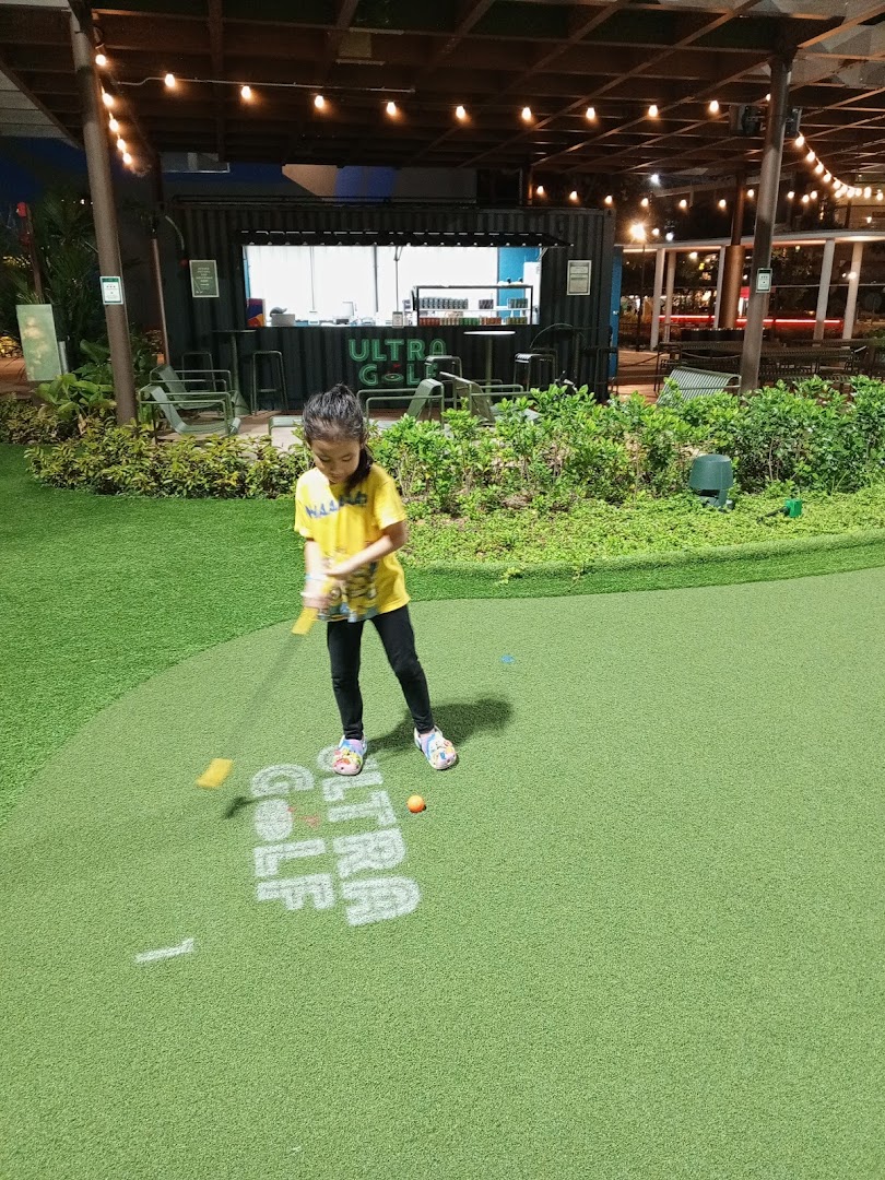 A young girl plays mini-golf at UltraGolf, with the shop's container-style counter in the background.